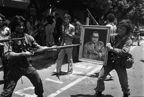 Un guerrillero apuntando con su arma un retrato del dictador Anastasio Somoza Debayle, en señal de celebración.