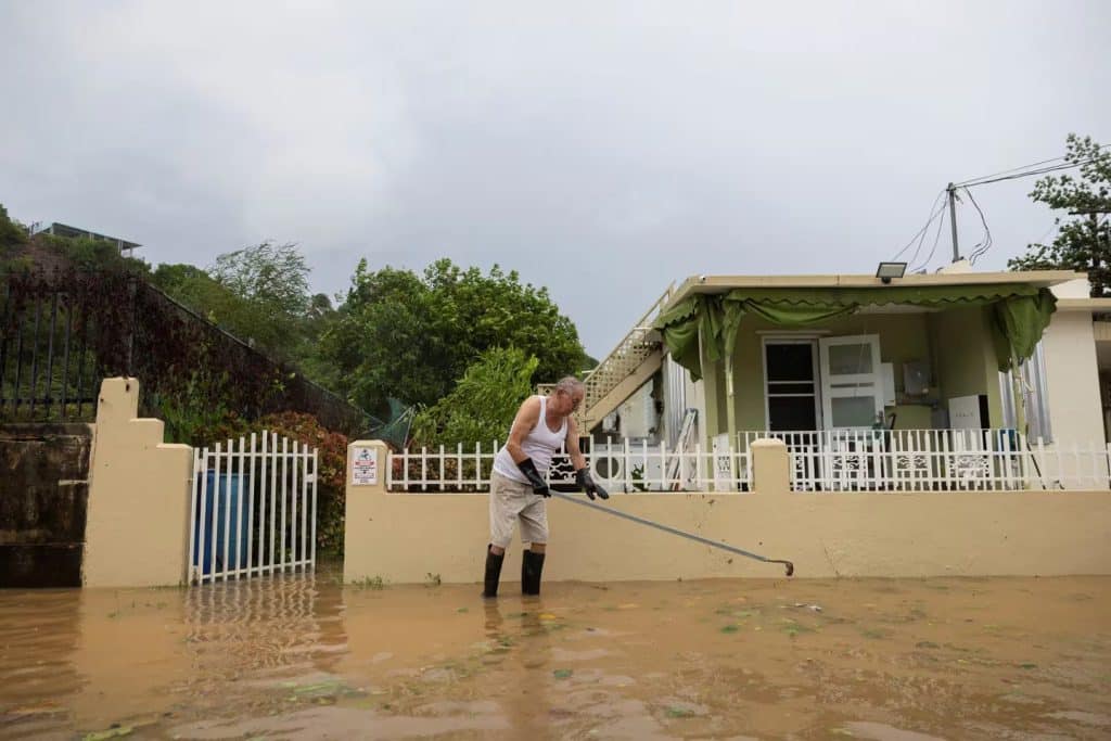 Ciudadano de 80 años intentando destapar el drenaje de su residencia, tras el paso del huracán Ernesto.