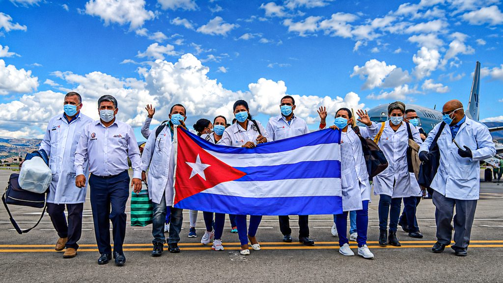 Brigadistas cubanos sostienen la bandera de Cuba en una pista de aeropuerto.