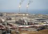 Irán descubre una gigantesca reserva de gas y refuerza su potencial energético Complejo petrolero costero con tanques, tuberías y antorchas de gas encendidas.