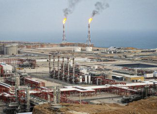 Irán descubre una gigantesca reserva de gas y refuerza su potencial energético Complejo petrolero costero con tanques, tuberías y antorchas de gas encendidas.