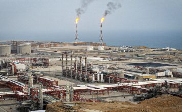 Irán descubre una gigantesca reserva de gas y refuerza su potencial energético Complejo petrolero costero con tanques, tuberías y antorchas de gas encendidas.