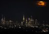 Eclipse lunar parcial iluminará el cielo de Estados Unidos Eclipse lunar de tonalidad rojiza sobre el horizonte iluminado de una ciudad de Estados Unidos.