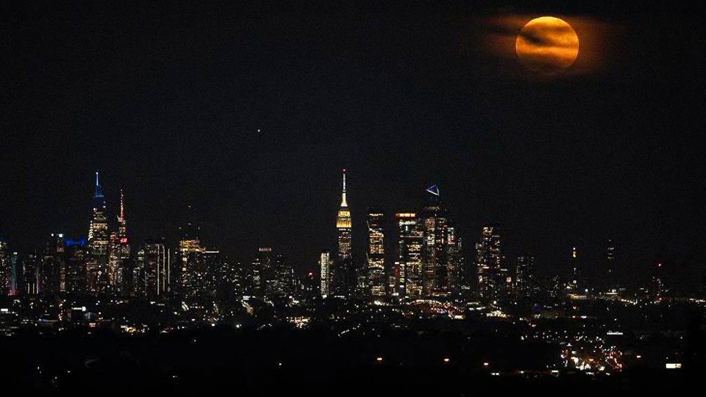 Eclipse lunar de tonalidad rojiza sobre el horizonte iluminado de una ciudad de Estados Unidos.