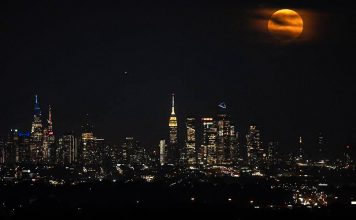 Eclipse lunar parcial iluminará el cielo de Estados Unidos Eclipse lunar de tonalidad rojiza sobre el horizonte iluminado de una ciudad de Estados Unidos.