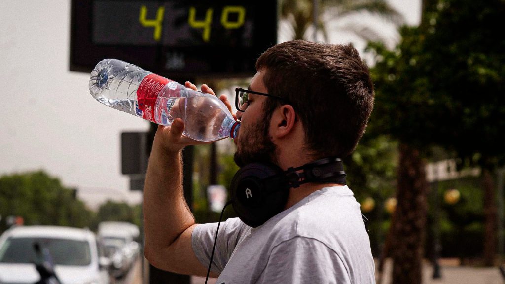 Hombre bebe agua mientras un termómetro marca 44 grados.