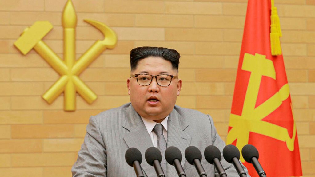 Kim Jong-un pronuncia un discurso de Año Nuevo frente a micrófonos y banderas de Corea del Norte.