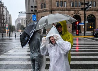 China refuerza respuesta de emergencia ante tifones y tormentas Personas cruzan una calle de China bajo una intensa lluvia con paraguas y ponchos.