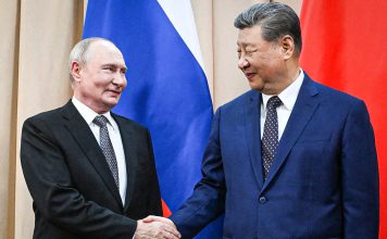 Organización de Shanghái reúne a líderes de Eurasia en Kirguistán Vladímir Putin y Xi Jinping se estrechan la mano frente a las banderas de Rusia y China.
