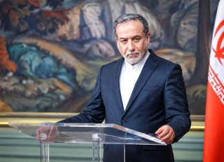 Araqchi “besaría la mano” de quien ejecute a Trump Funcionario iraní durante una comparecencia oficial junto a la bandera de Irán.