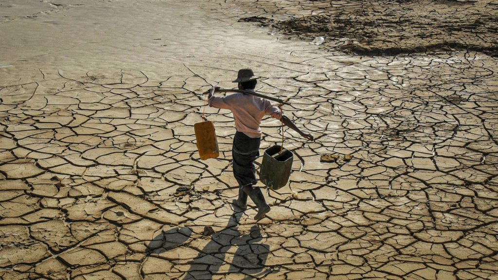 Hombre busca agua mientras camina sobre suelo agrietado por la sequía.