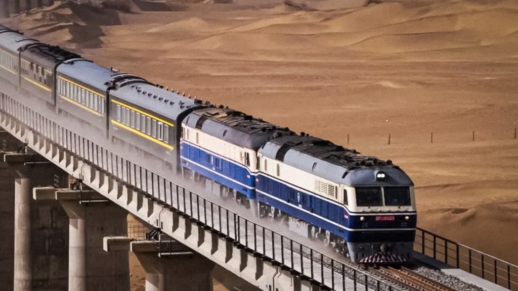 Tren de carga con contenedores circula por un puente en una zona desértica.