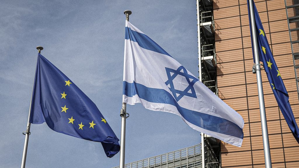Banderas de la Unión Europea e Israel ondean frente a un edificio institucional.