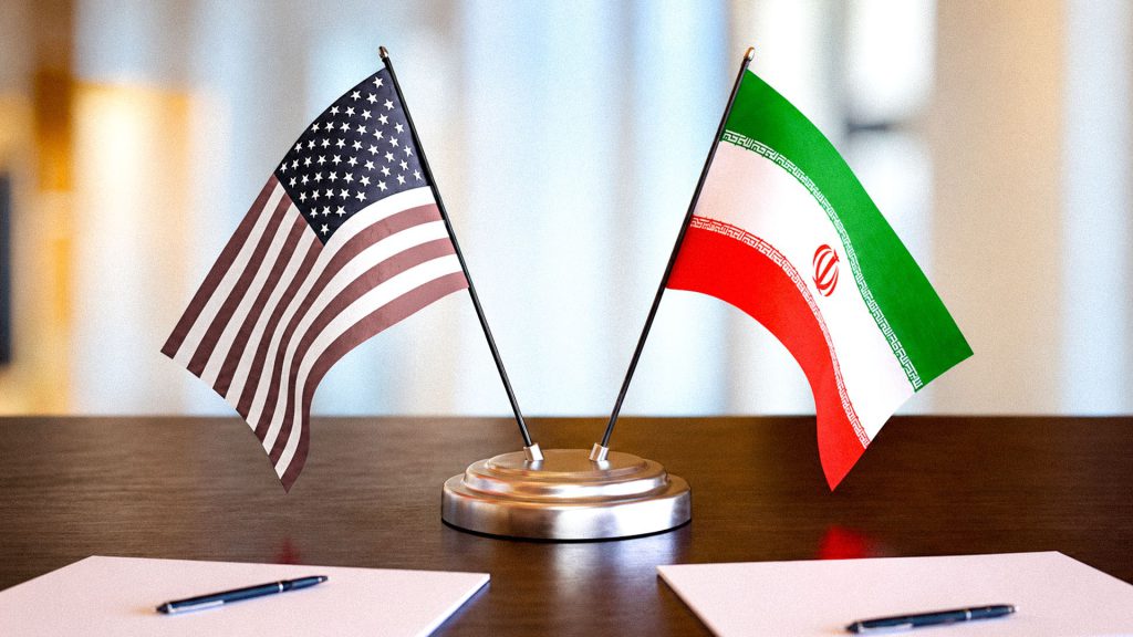 Imagen de referencia: Banderas de Estados Unidos e Irán sobre mesa de acuerdos diplomáticos