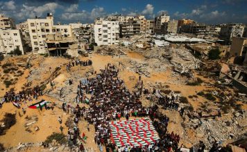 Palestina: Condenamos la continua campaña genocida librada por Israel Palestinos participan en un funeral entre edificios destruidos en Gaza.