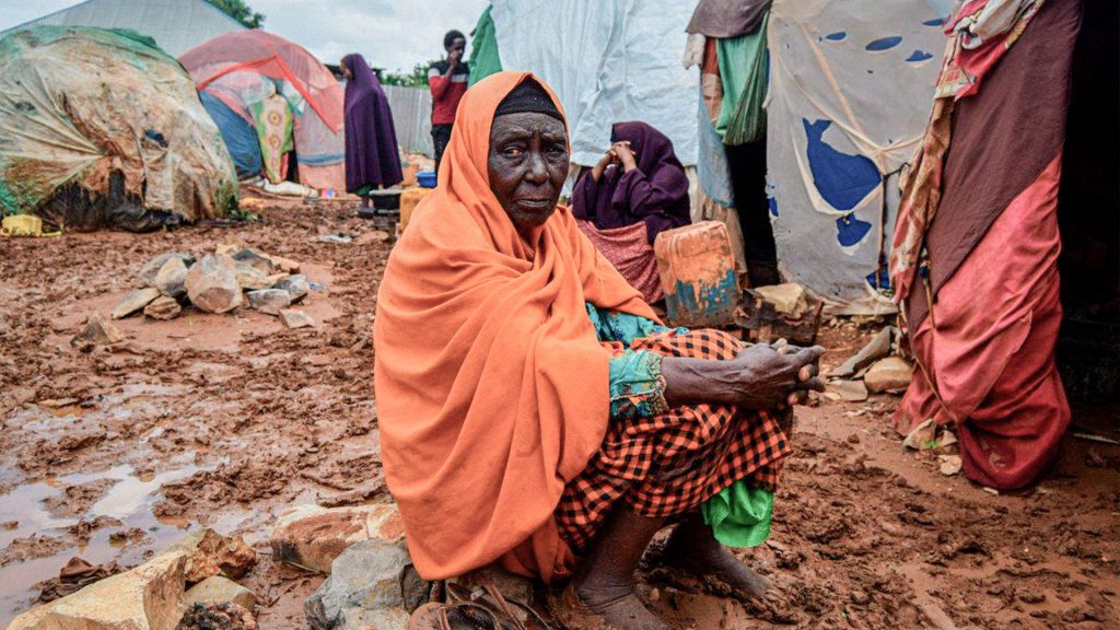 Mujer en un asentamiento de desplazados en Somalia, rodeada de tiendas de campaña y suelo embarrado.