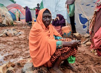 Inundaciones en Somalia amenazan con desplazar a más de 874.000 personas Mujer en un asentamiento de desplazados en Somalia, rodeada de tiendas de campaña y suelo embarrado.