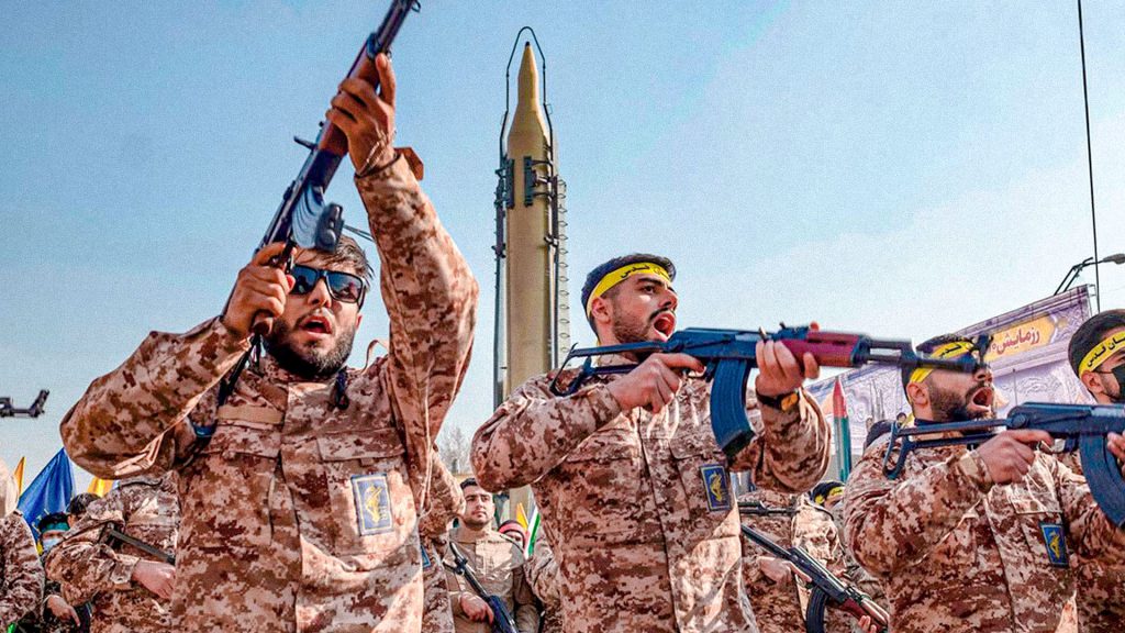 Militares iraníes armados durante una exhibición militar con un misil al fondo.