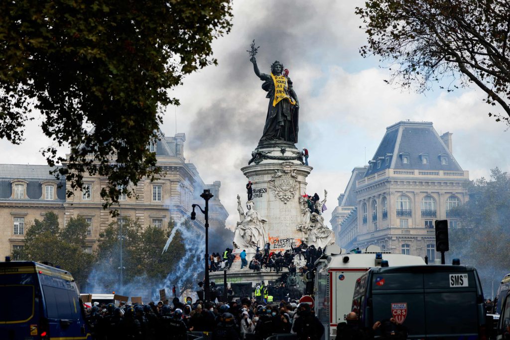 Manifestantes y fuerzas policiales durante protestas en la plaza de la República, en París, entre humo y vehículos policiales.
